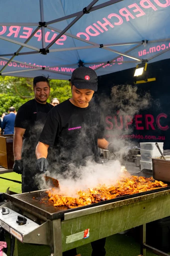 Superchido chef cooking marinated meat on a flat-top grill at an outdoor event